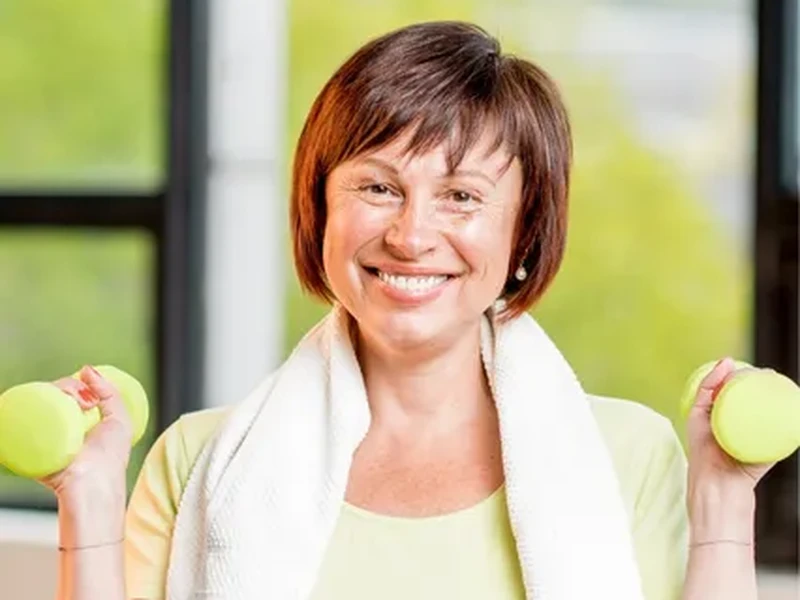 A smiling woman holding light dumbbells after finishing her recovery program